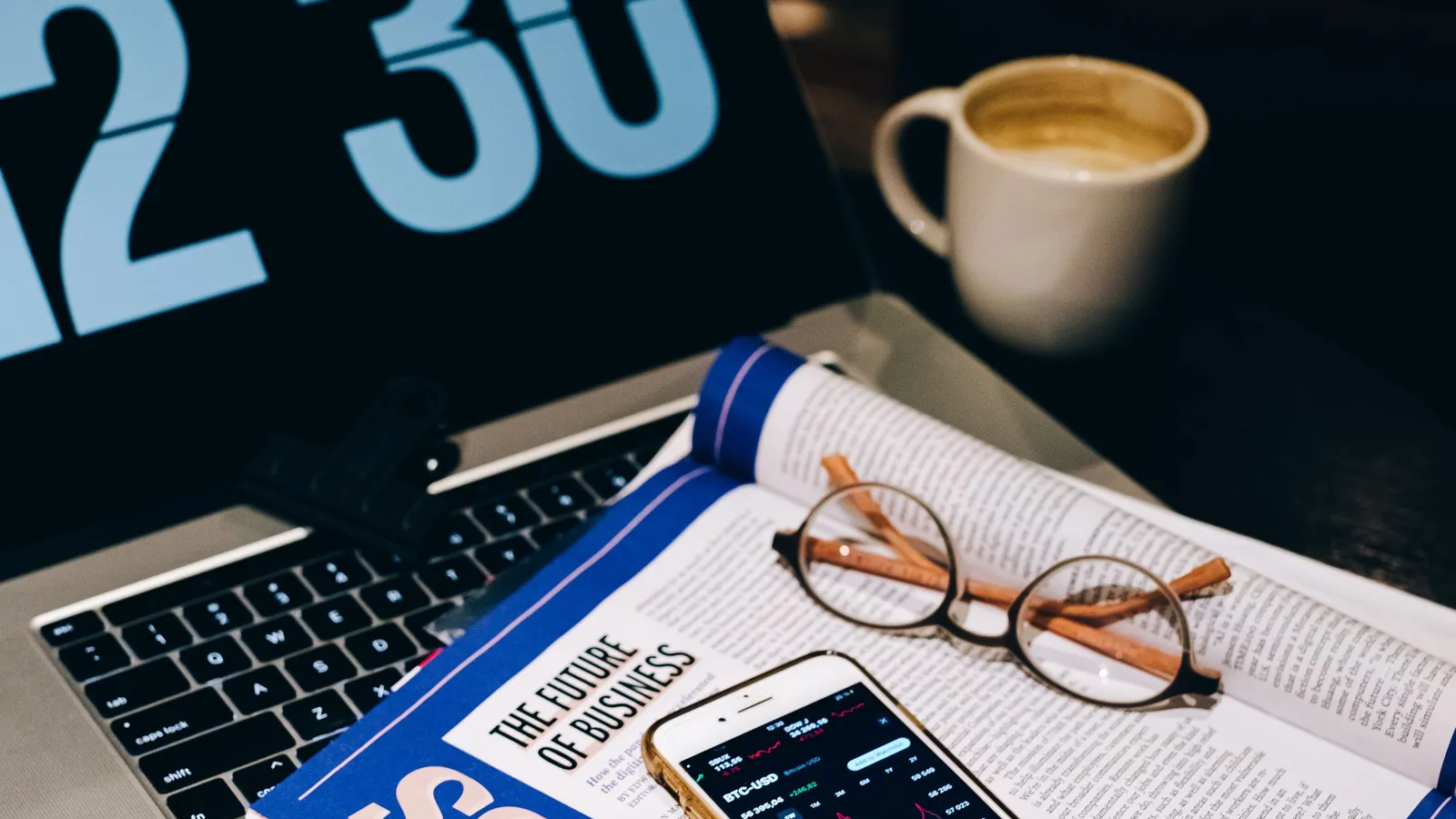 Newsletter printout, smartphone and eyeglasses resting on a laptop keyboard