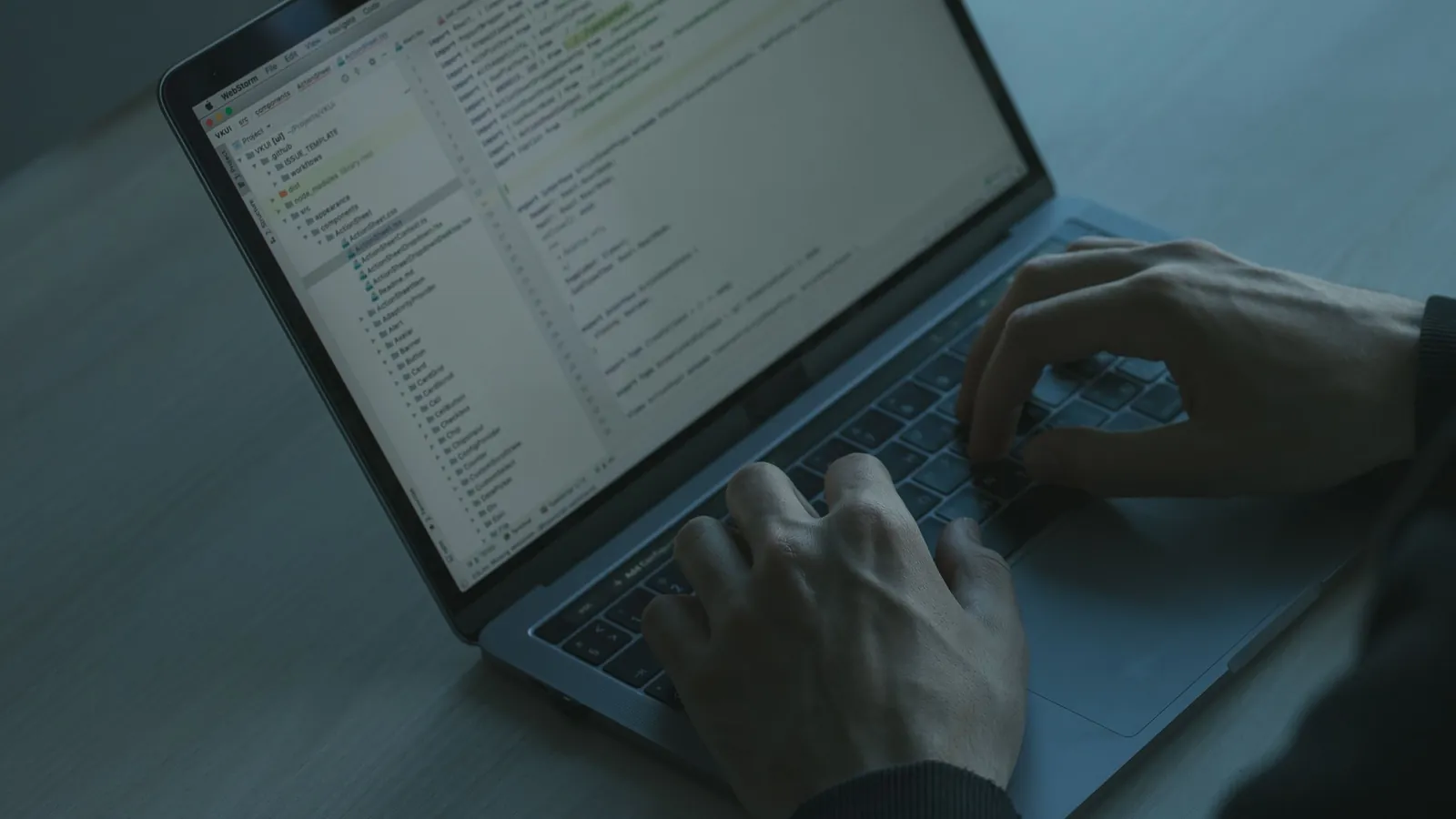 Hands typing on a laptop keyboard in a dimly lit room