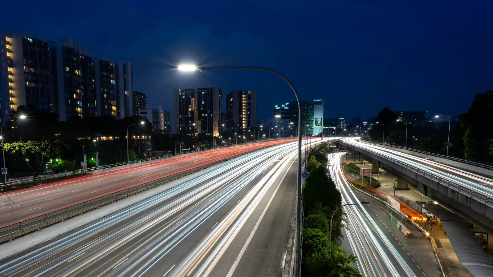 Long-exposure light trails on a Singapore expressway at night, with residential blocks and street lights